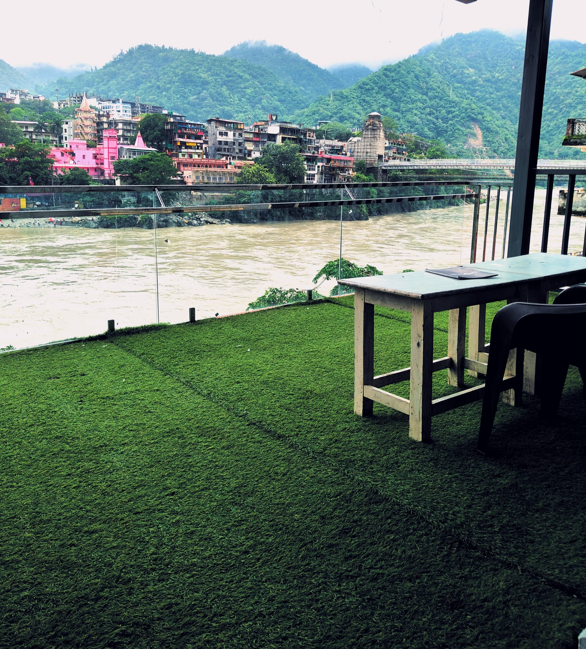 Panoramic view from Hotel Ganga View terrace overlooking the Ganges River, Rishikesh town, green mountains, and Laxman Jhula.