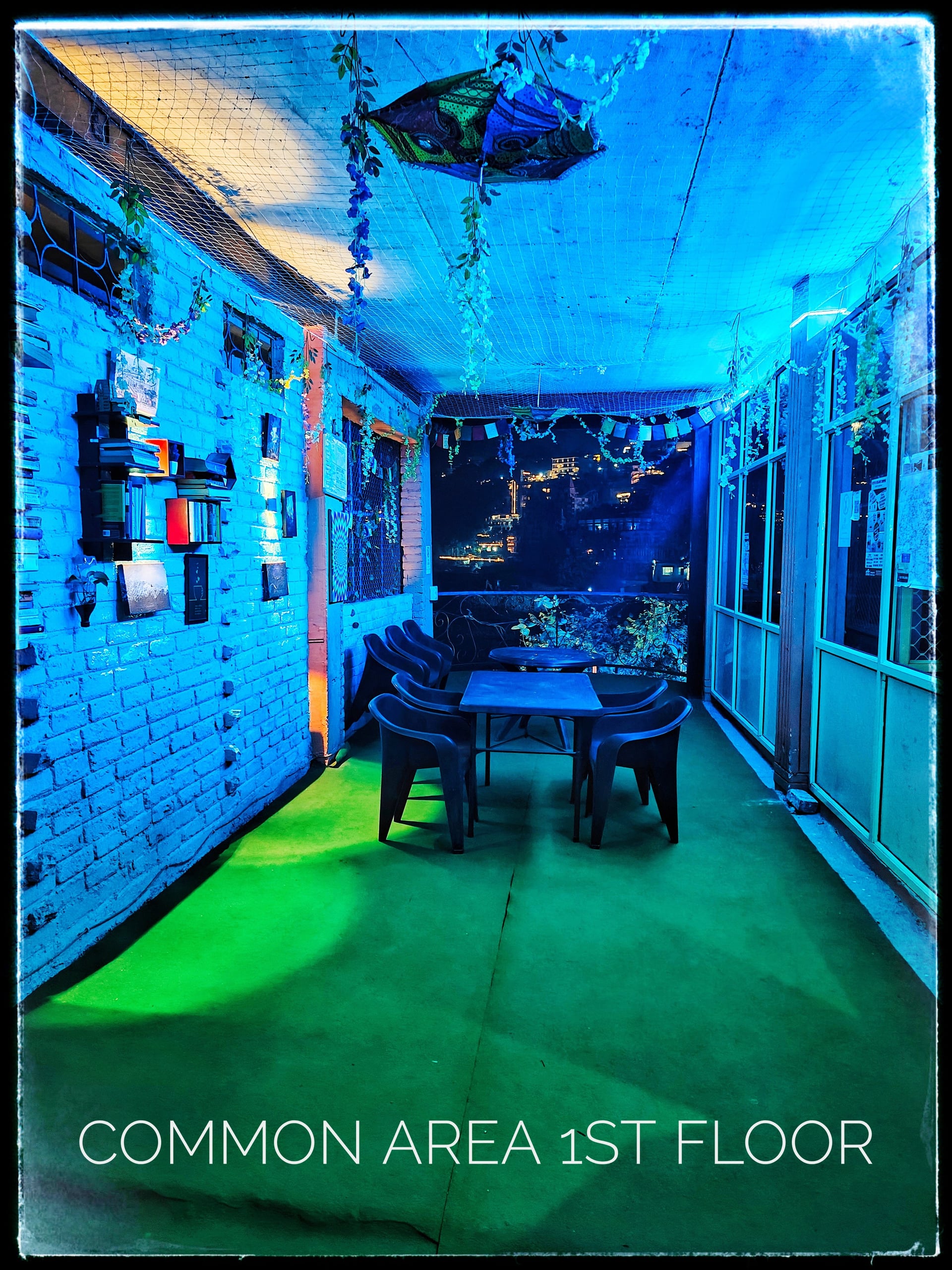 Night view of the hotel's 1st-floor common area with blue and green lighting, outdoor seating, and city lights in the distance.