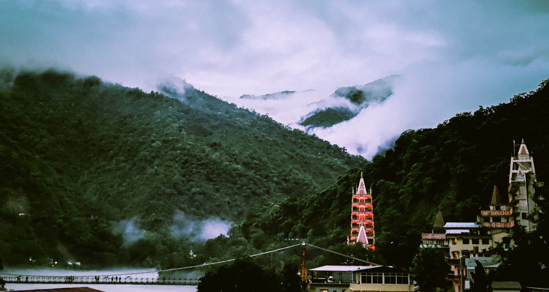 Misty green mountains overlooking the holy Ganga River with Laxman Jhula bridge and traditional temples in Rishikesh.