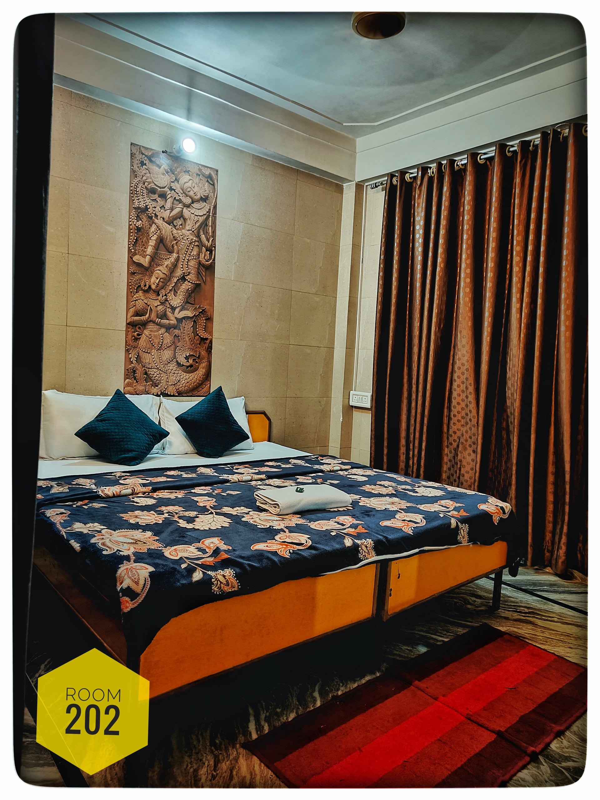 Room 202 at Hotel Ganga View with a large bed, patterned blue and white duvet, blue pillows, and a traditional carved wall decoration.