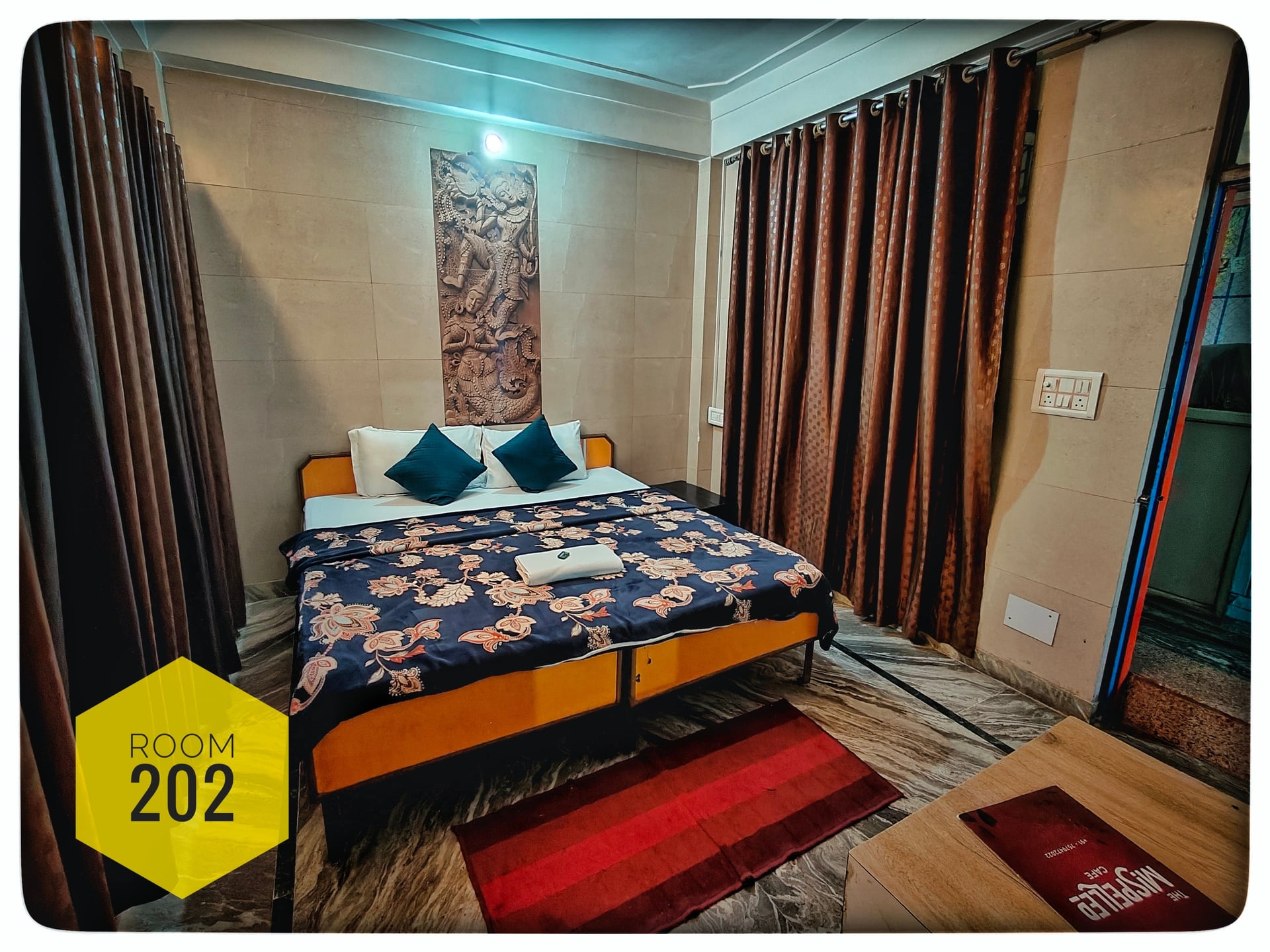 Hotel Ganga View double bedroom with patterned blue and orange bedding, two blue pillows, and a decorative wall carving above the bed.