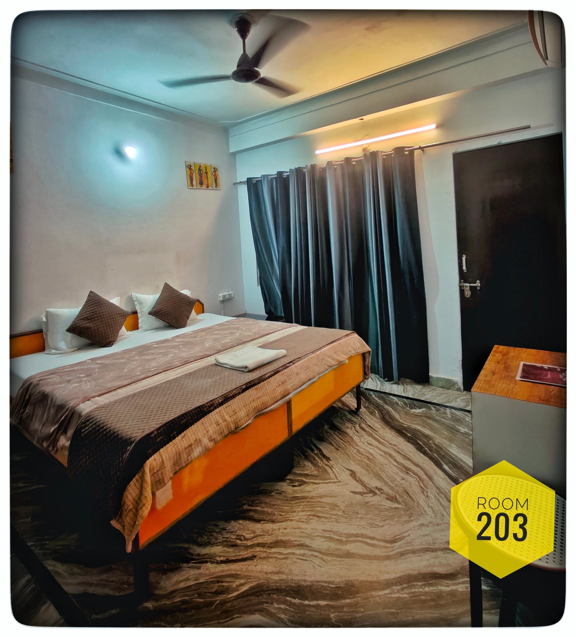 Hotel Ganga View Room 203 featuring a comfortable double bed, ceiling fan, and dark curtains, with patterned marble flooring.