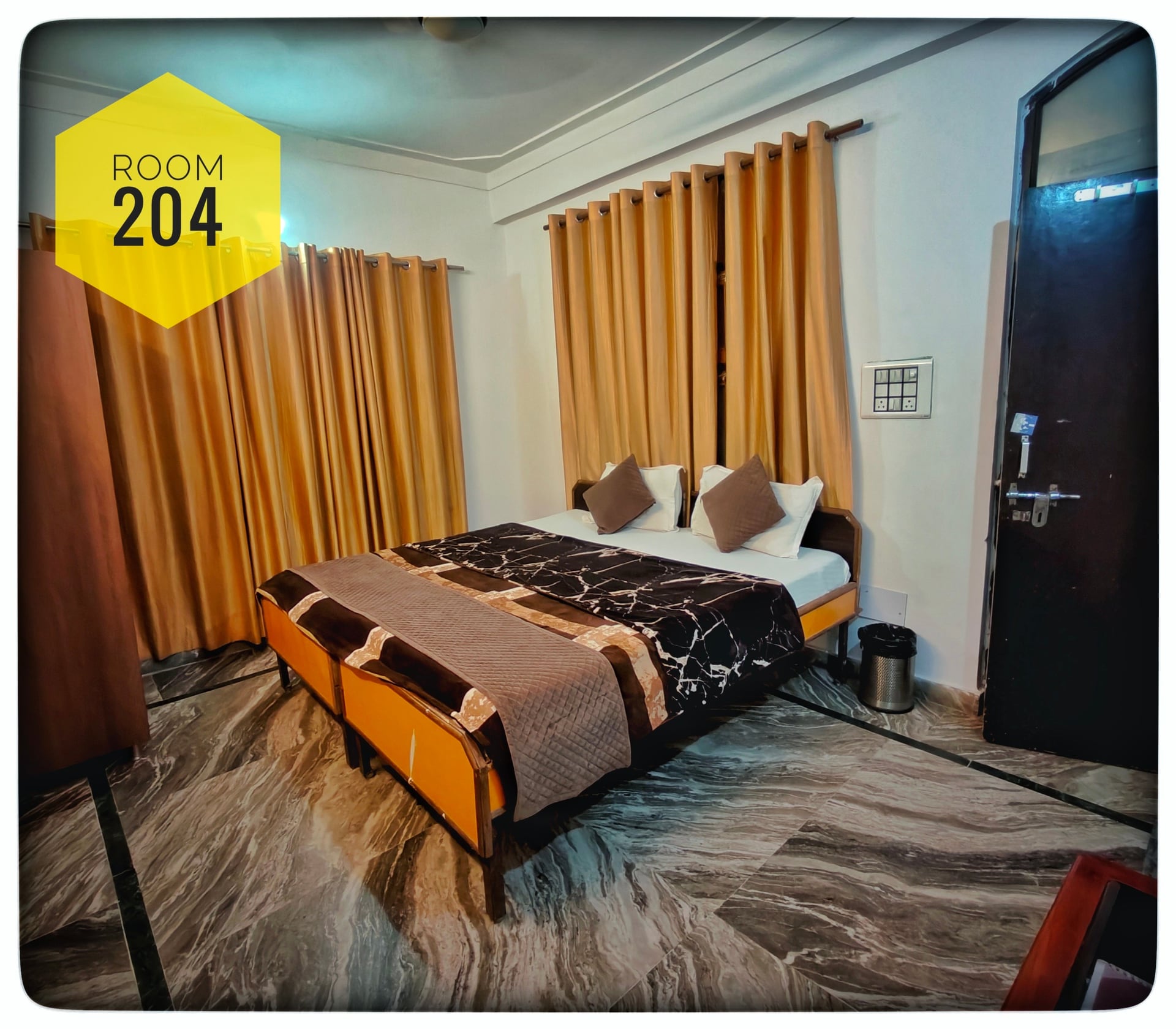 Room 204 at Hotel Ganga View with a double bed, brown and white bedding, golden curtains, and marble-patterned floor.