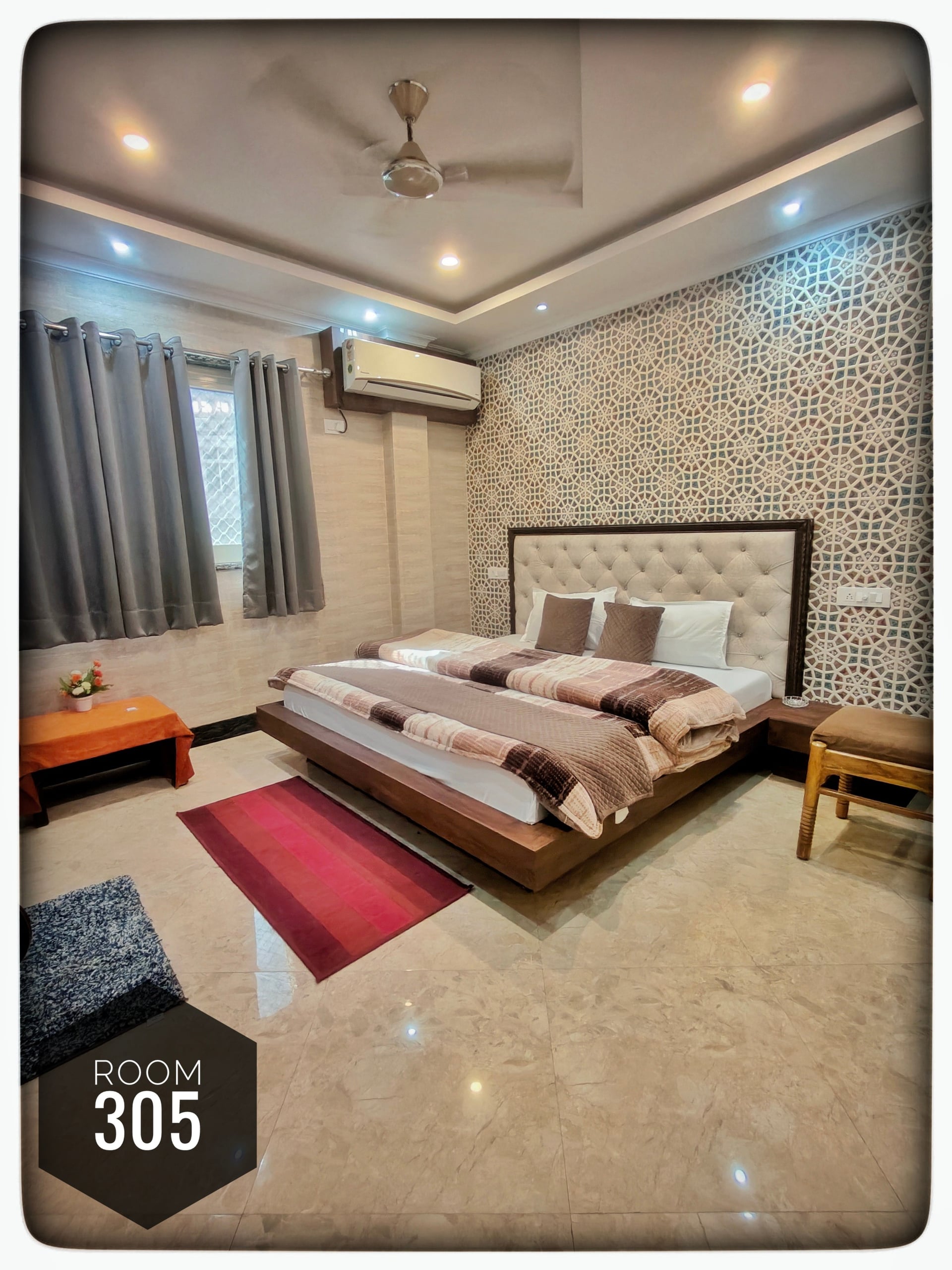 Comfortable double bedroom 305 at Hotel Ganga View with a large bed, patterned accent wall, AC, ceiling fan, and tiled floor.