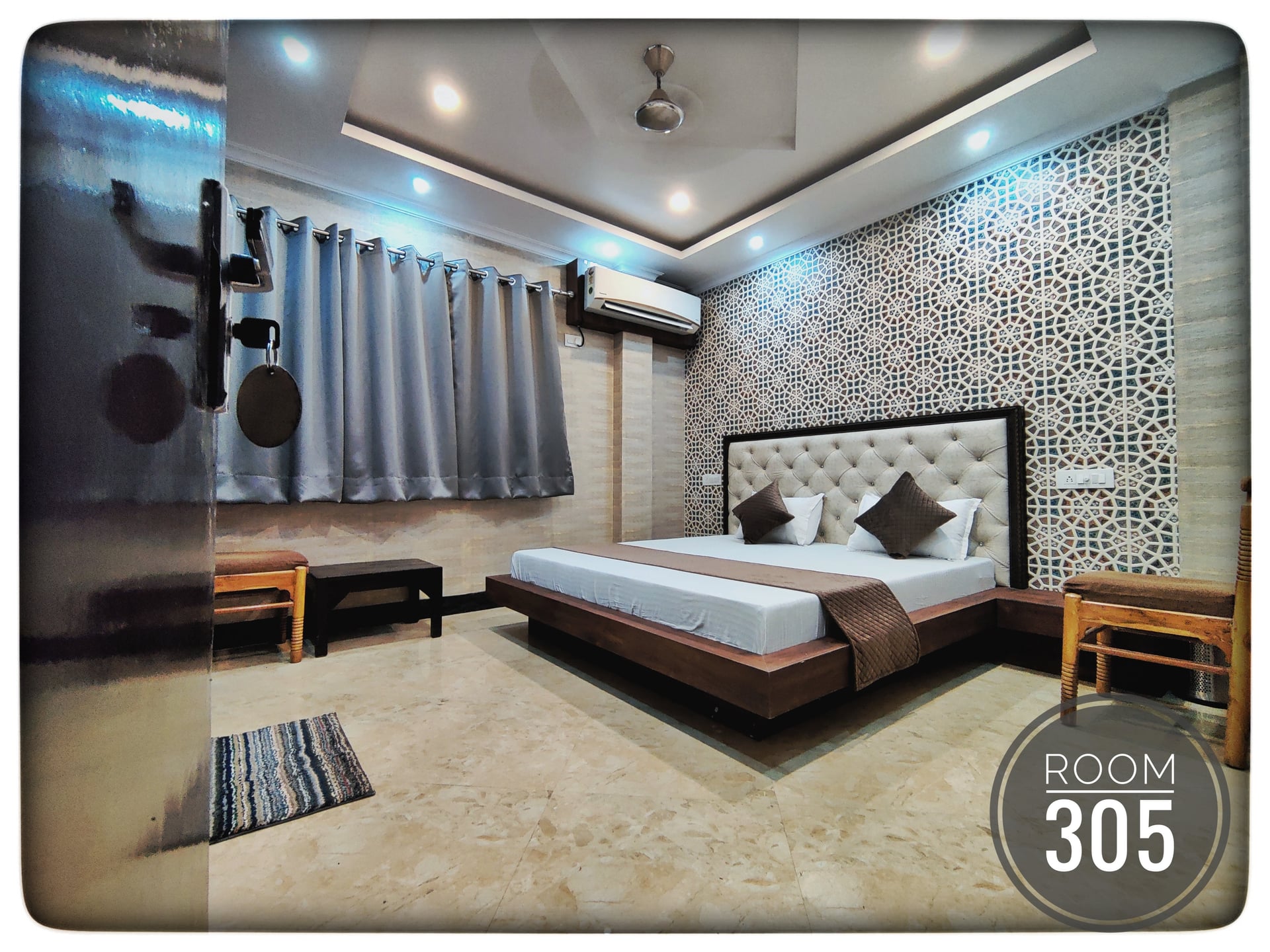 Hotel Ganga View Room 305 featuring a large bed with a tufted headboard and a patterned accent wall, modern decor, ceiling fan, and AC.