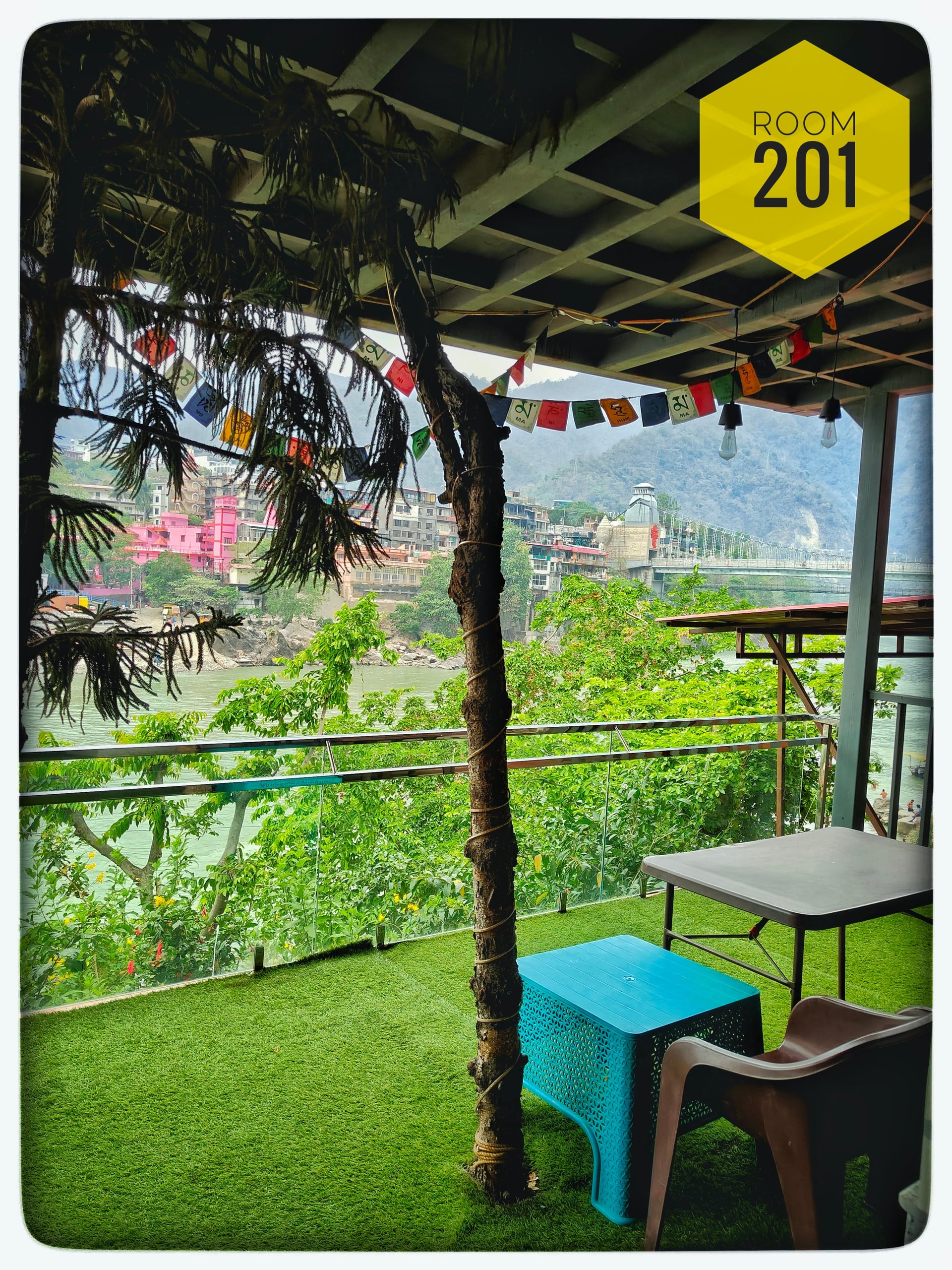 Balcony of Room 201 with artificial turf, outdoor seating, and panoramic view of the Ganges River and Laxman Jhula bridge.
