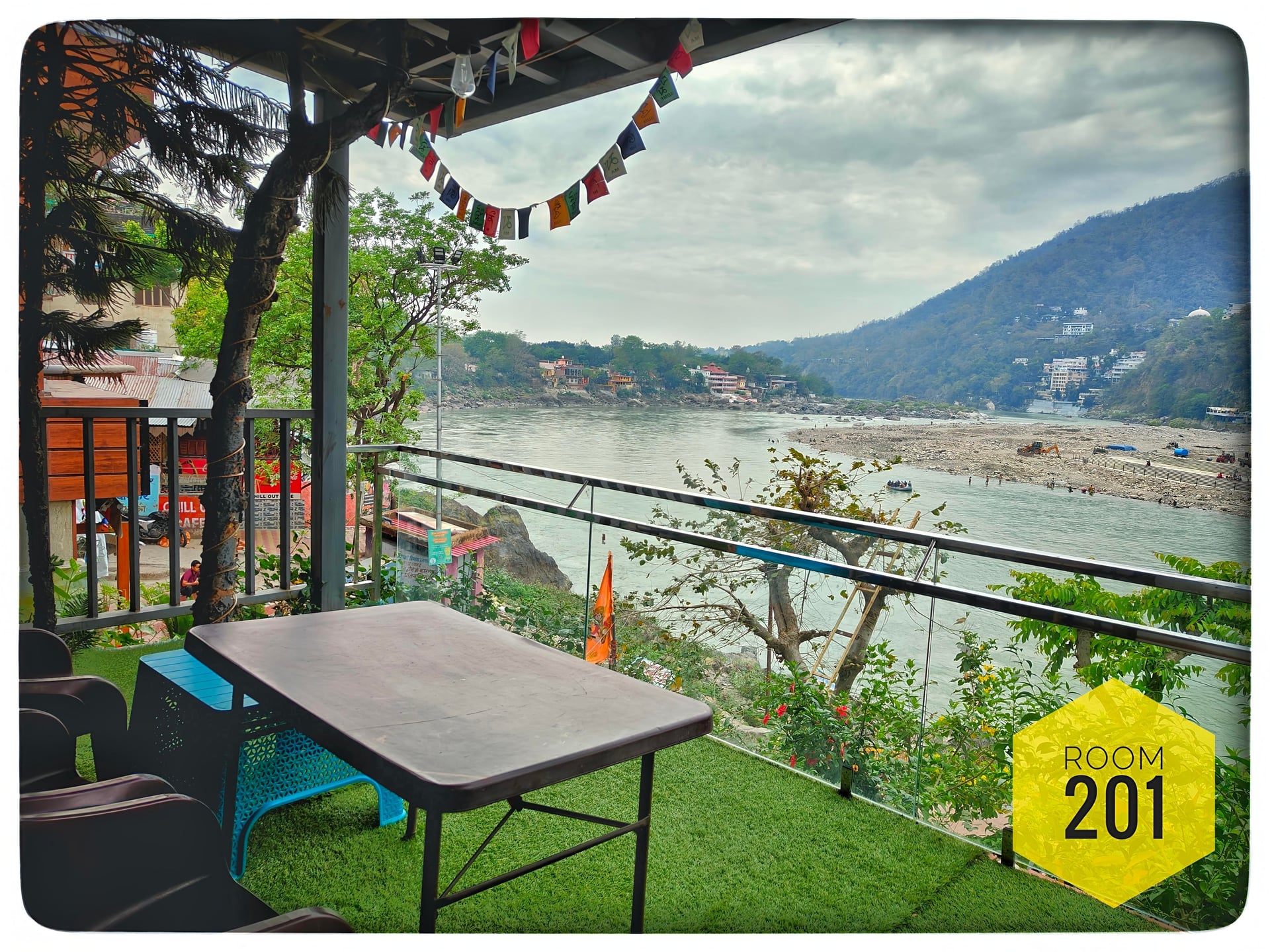 Room 201 private balcony with outdoor seating, artificial grass, and a panoramic view of the Ganga River and Himalayan mountains.