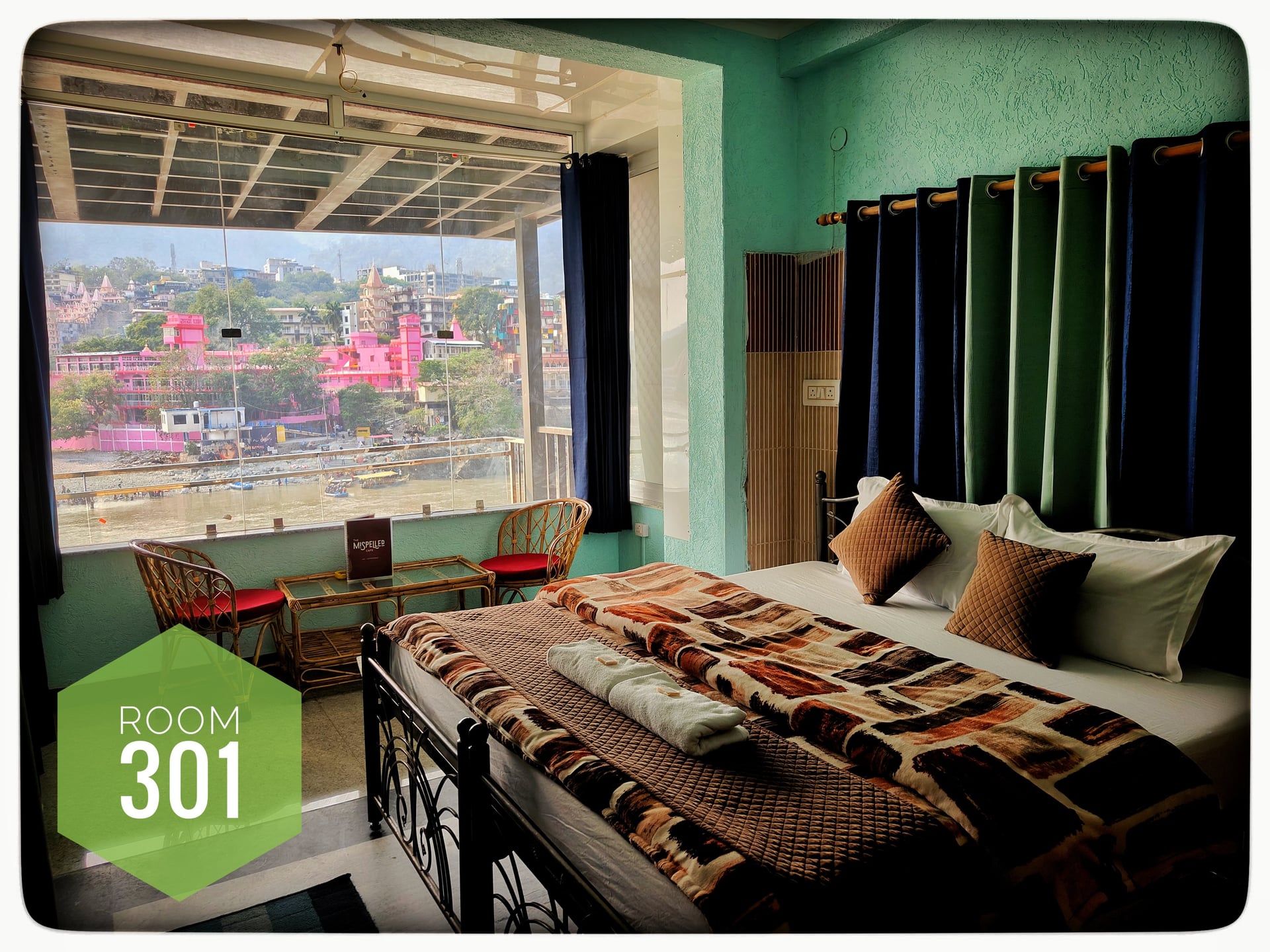 Hotel room 301 with a comfortable bed, large window overlooking the Ganga River, and a small balcony seating area.
