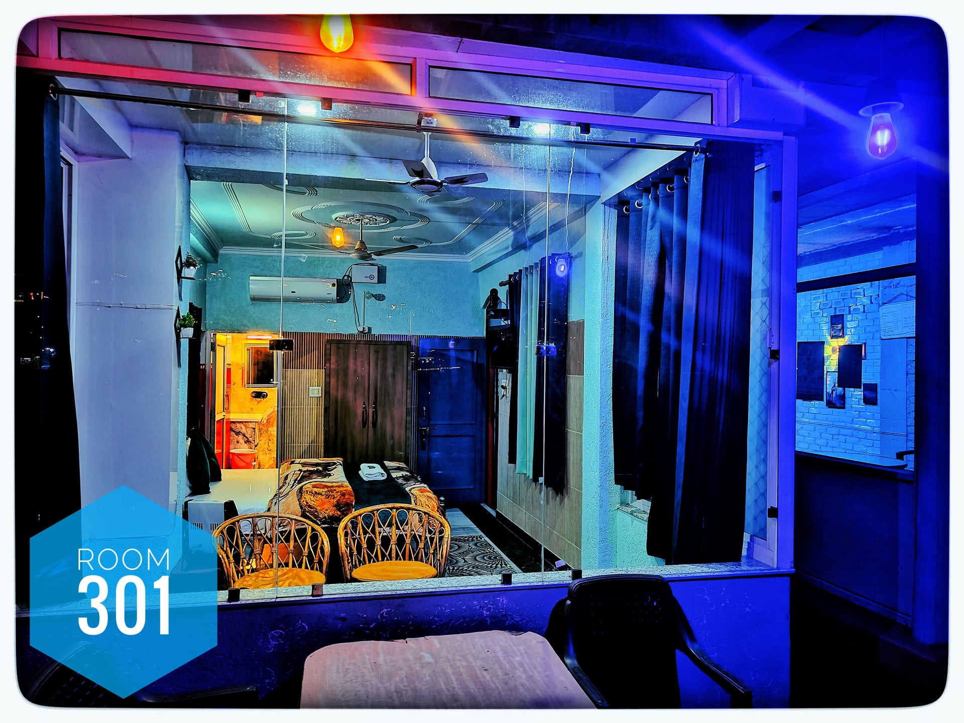 Hotel Ganga View Room 301, a bedroom with a double bed, two wicker chairs, and blue ambient lighting.