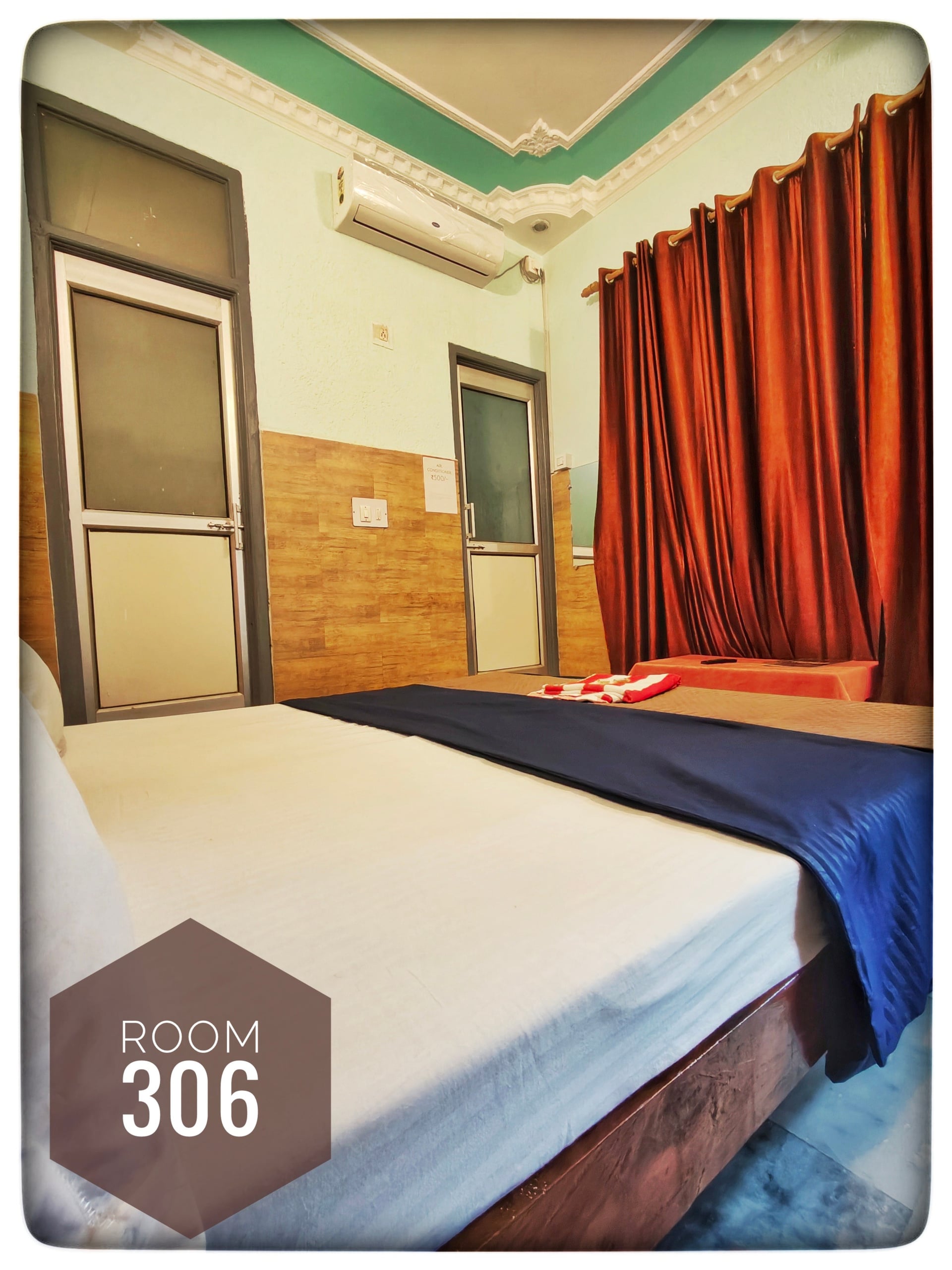 Standard hotel Room 306 with white bed, blue runner, air conditioning, and two doors. Walls are light green and wood paneling.
