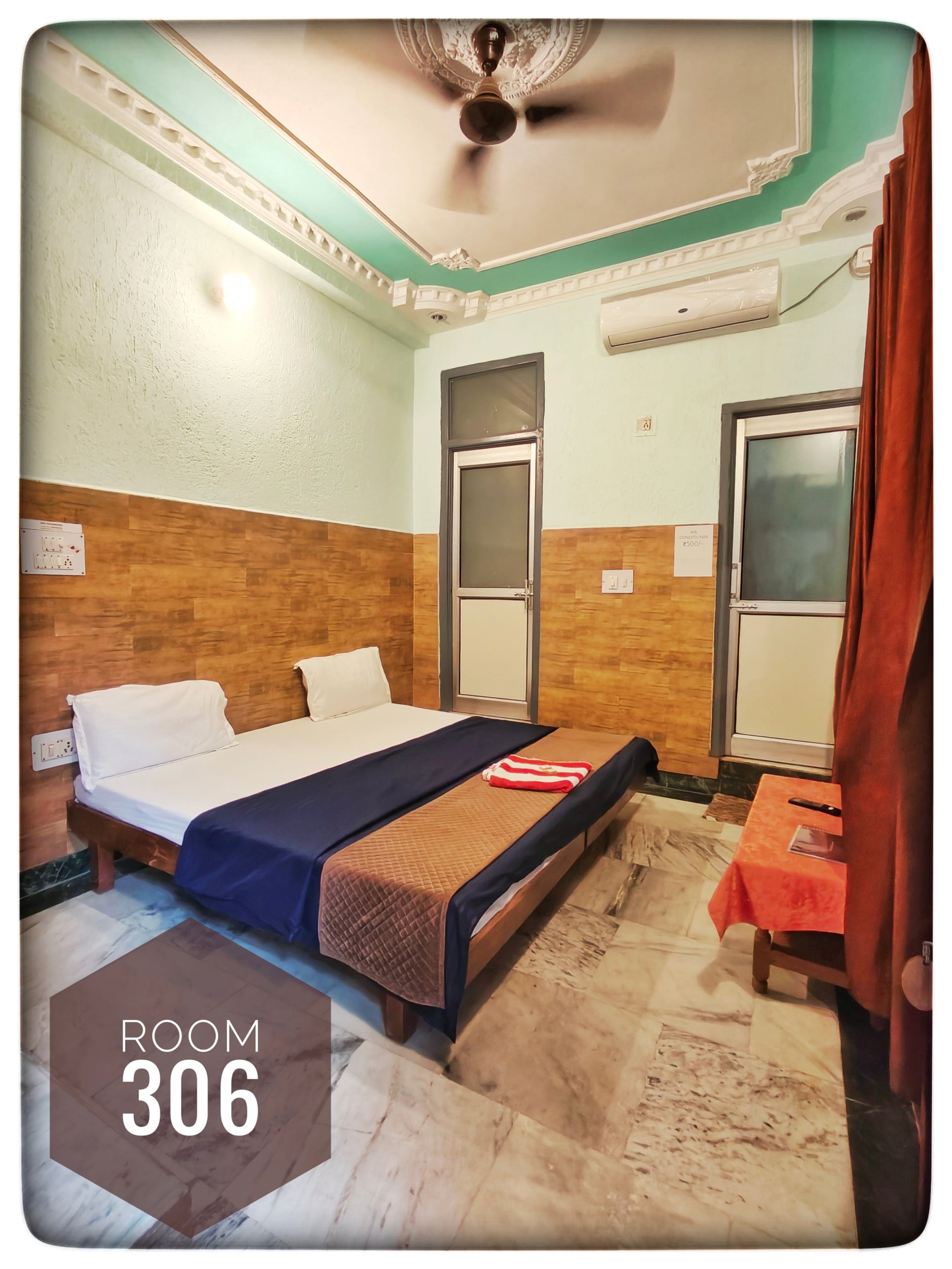 Hotel Ganga View Room 306 with two single beds, blue and brown linens, light green walls, wooden paneling, ceiling fan, and AC.