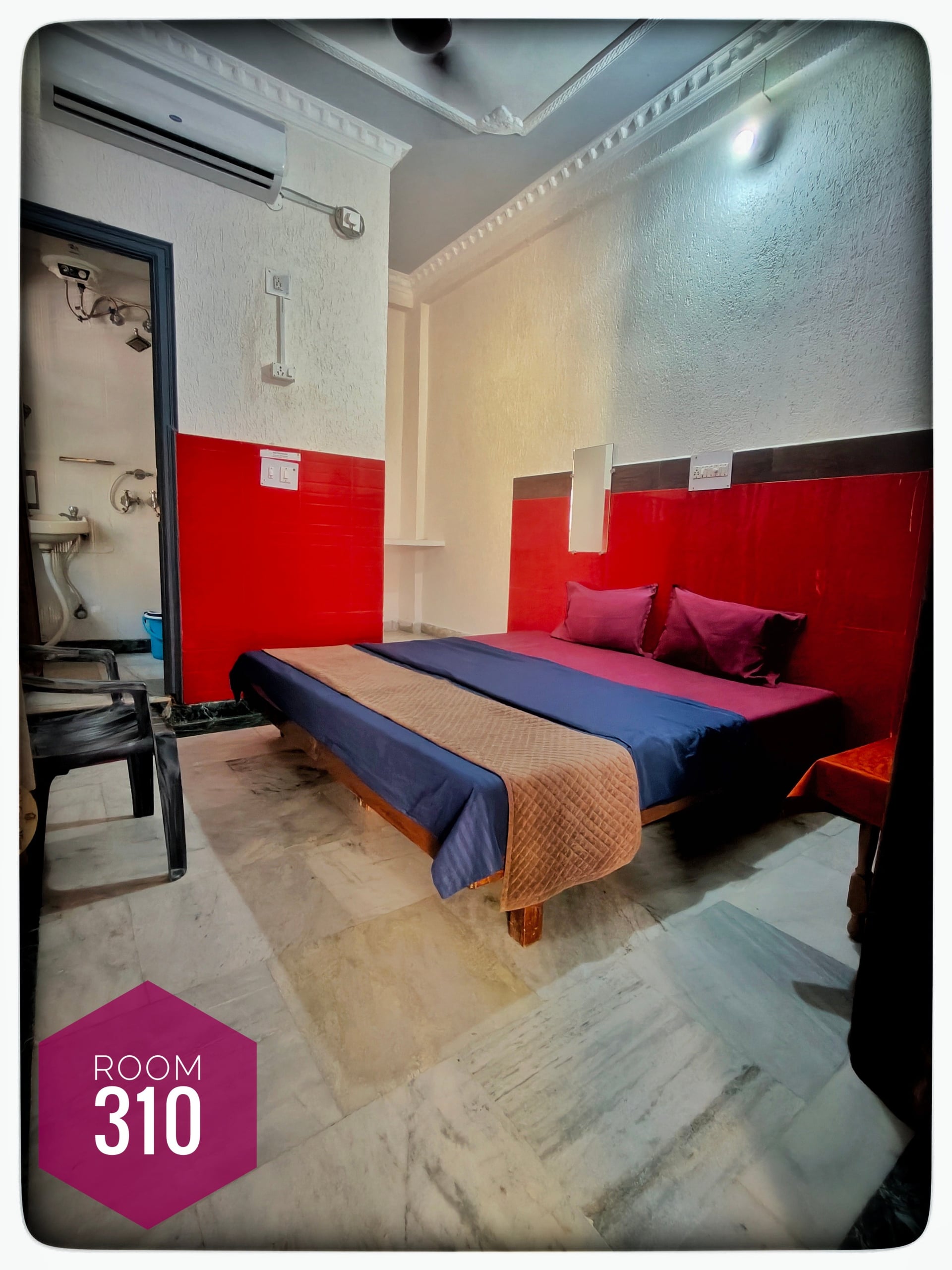 Hotel Ganga View Room 310: Bedroom with a bed, blue and brown bedding, red headboard, marble floor, and a bathroom entrance.