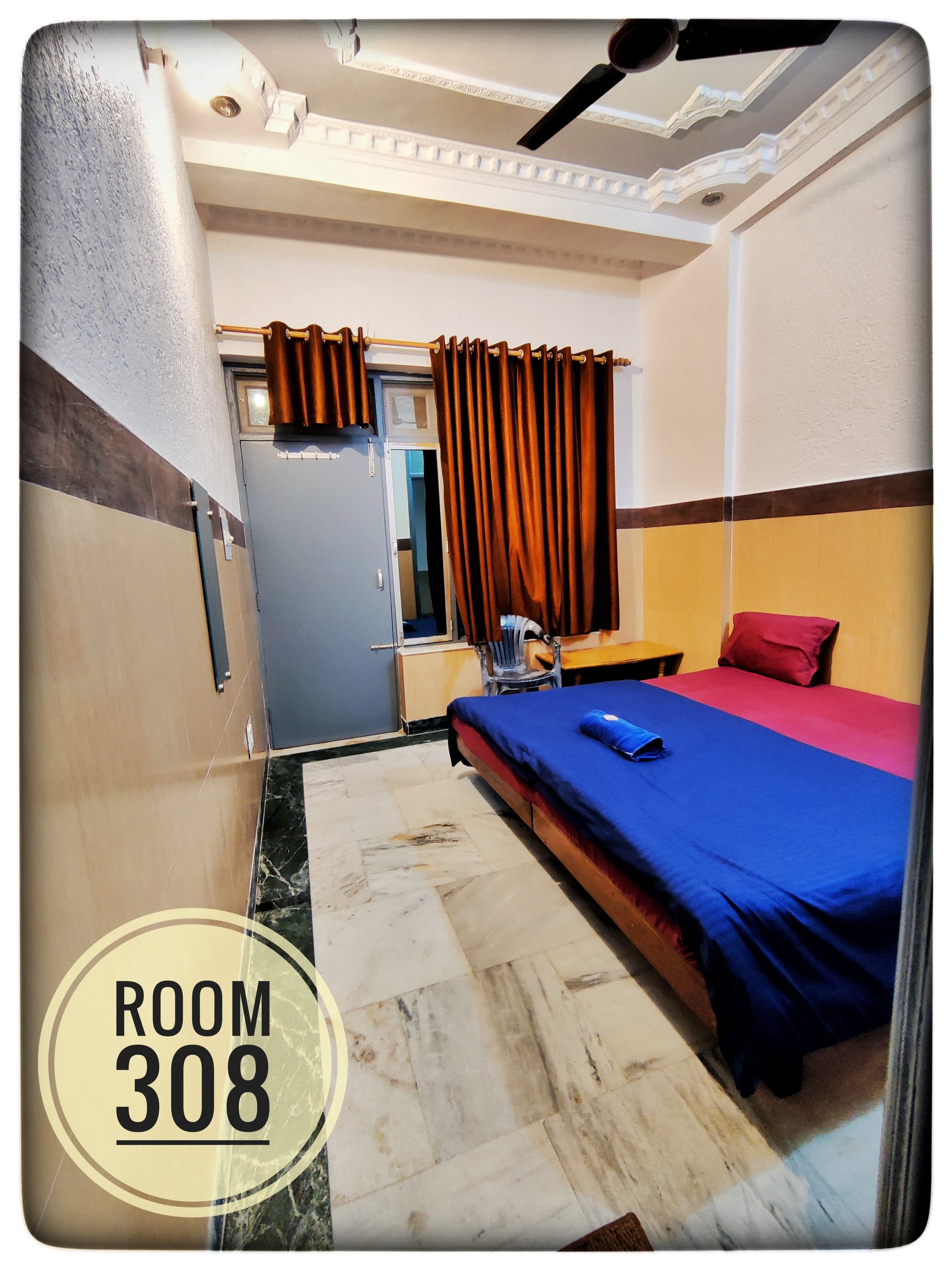 Standard single bedroom in Hotel Ganga View with a bed, blue bedding, ceiling fan, marble floor, and window with brown curtains.
